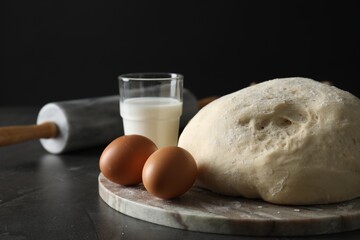 Raw dough, rolling pin and ingredients on black table, closeup