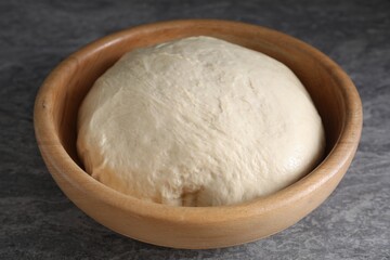 Raw dough in bowl on grey table, closeup