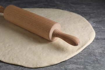 Raw dough and rolling pin on grey table