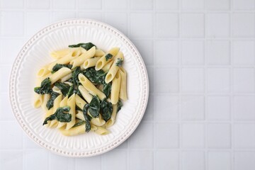 Tasty pasta with spinach and sauce on white tiled table, top view. Space for text
