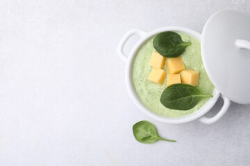 Delicious spinach cream soup with cheese in bowl on light grey table, top view. Space for text