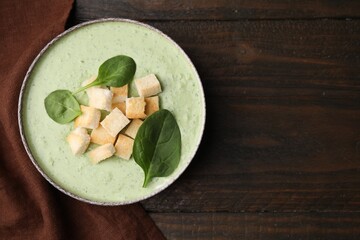 Delicious spinach cream soup with leaves and croutons in bowl on wooden table, top view. Space for text