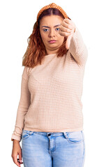Obraz premium Young latin woman wearing casual clothes and diadem looking unhappy and angry showing rejection and negative with thumbs down gesture. bad expression.