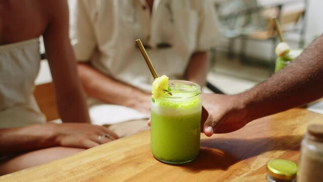 Waiter hand putting fruit smoothies with straws on wooden table to couple in love in cafe on Bali. Hand of waiter delivering healthy drinks to the customers. Man and woman getting beverages. Close-up.