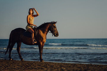 Woman riding a horse during a sunset and looking away and lifting sunglasses