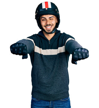 Young hispanic man with beard wearing motorcycle helmet doing driving gesture winking looking at the camera with sexy expression, cheerful and happy face.