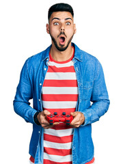 Young hispanic man with beard playing video game holding controller afraid and shocked with surprise and amazed expression, fear and excited face. © Krakenimages.com