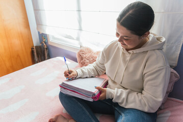 Young woman sitting on bed and writing in a diary at home. Concept of education