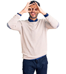 Fototapeta premium Young handsome hispanic man wearing elegant clothes and glasses doing ok gesture like binoculars sticking tongue out, eyes looking through fingers. crazy expression.