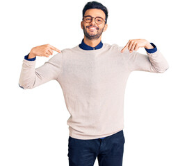 Naklejka premium Young handsome hispanic man wearing elegant clothes and glasses looking confident with smile on face, pointing oneself with fingers proud and happy.