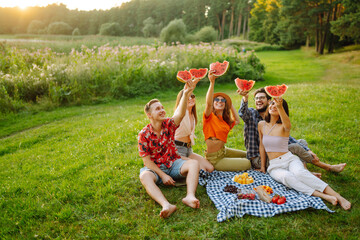 Cheerful friends eating fruits while sitting on the park. Young people having fun in summer...