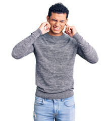 Fototapeta premium Hispanic handsome young man wearing casual sweater covering ears with fingers with annoyed expression for the noise of loud music. deaf concept.