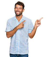 Handsome young man with beard wearing casual fresh shirt smiling and looking at the camera pointing with two hands and fingers to the side.