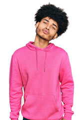 Young african american man with afro hair wearing casual pink sweatshirt looking at the camera blowing a kiss on air being lovely and sexy. love expression.