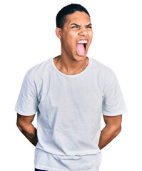 Young hispanic man wearing casual white t shirt angry and mad screaming frustrated and furious, shouting with anger. rage and aggressive concept.