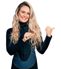 Young blonde woman wearing diver neoprene uniform pointing to the back behind with hand and thumbs...
