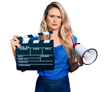 Young blonde woman holding video film clapboard and megaphone skeptic and nervous, frowning upset because of problem. negative person.
