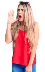 Young beautiful blonde woman wearing sleeveless t-shirt and sunglasses shouting and screaming loud to side with hand on mouth. communication concept.