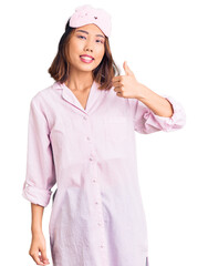 Young beautiful chinese girl wearing sleep mask and pajama doing happy thumbs up gesture with hand. approving expression looking at the camera showing success.