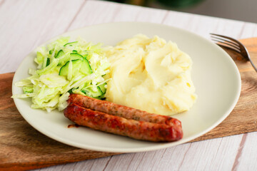Wholesome dinner: Sausages, mashed potatoes, and fresh cabbage salad with cucumbers presented on a...