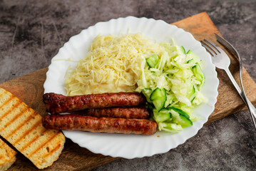 A delicious plate featuring sausages, creamy mashed potatoes, and a side of coleslaw salad,...