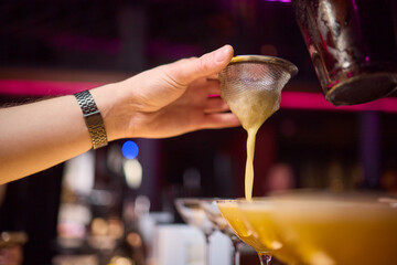 Bartender pours pink cocktail into martini glass with flair