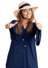 Middle age hispanic woman wearing summer hat approving doing positive gesture with hand, thumbs up smiling and happy for success. winner gesture.