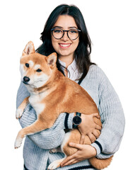 Beautiful hispanic woman holding cute dog smiling with a happy and cool smile on face. showing teeth.