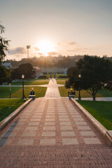 Wide, descending stairs lead to a lush lawn with a sports stadium and buildings in the background. UCLA Bruin Bear on the University of California, Los Angeles, campus.