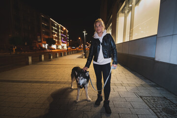 A young girl of European appearance walks with a husky dog ​​in the night city of Krakow in the...