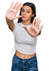 Young hispanic girl wearing casual white t shirt doing frame using hands palms and fingers, camera perspective