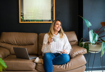 mujer ejecutiva sentada en el sofá tomando un café con su computadora al lado. 
