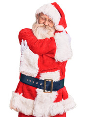 Old senior man with grey hair and long beard wearing traditional santa claus costume hugging oneself happy and positive, smiling confident. self love and self care