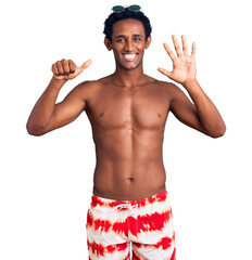 African handsome man wearing swimsuit and sunglasses showing and pointing up with fingers number...