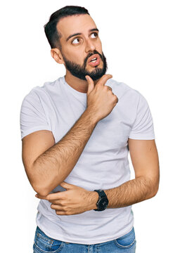 Young man with beard wearing casual white t shirt thinking worried about a question, concerned and nervous with hand on chin