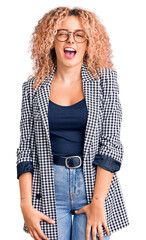 Young blonde woman with curly hair wearing business jacket and glasses winking looking at the...