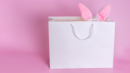 Funny Easter bunny ears in a white paper bag on a pink background.