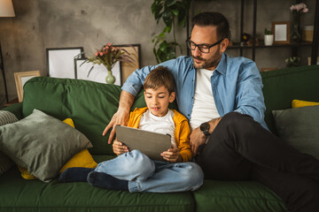Father look son while he play video games or browse internet on tablet