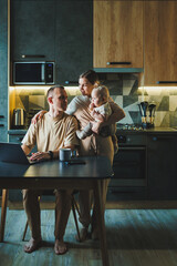 A young couple with a child in the kitchen. A man works at home on a laptop, and his wife with a...