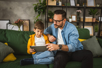 Father look son while he play video games or browse internet on tablet