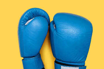 Blue boxing gloves isolated on yellow background. A pair of blue leather boxing gloves close-up top...