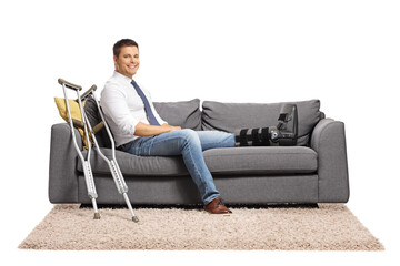 Businessman with a foot injury and leg brace sitting on a sofa