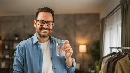 Portrait of adult caucasian man sit and hold glass of water at home