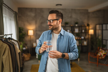 Portrait of adult caucasian man sit and hold glass of water at home