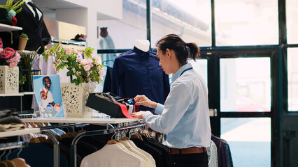 Asian store employee arranging trendy accessories, putting fashionable tie on shelf, working at...