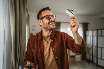 Portrait of adult man look at credit card hold mobile phone and smile