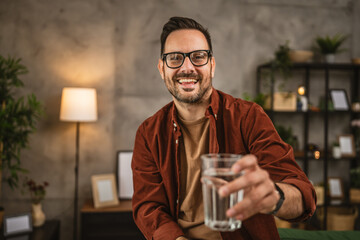 Portrait of adult caucasian man sit and hold glass of water at home