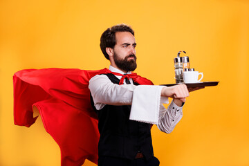 Elegant waiter with red cape carrying coffee on tray, having towel hanging over hand and posing as...