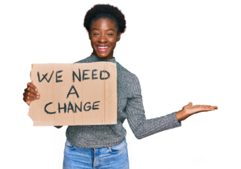 Young african american girl holding we need a change banner celebrating victory with happy smile and winner expression with raised hands