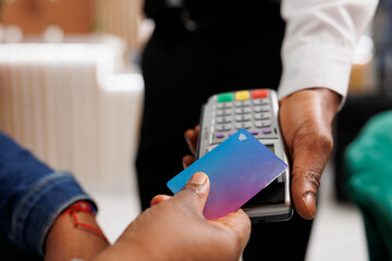 Close up of customer hand making NFC transaction holding credit card paying in hotel with contactless payment method. Traveler paying for hospitality services, electronic money, e-pay